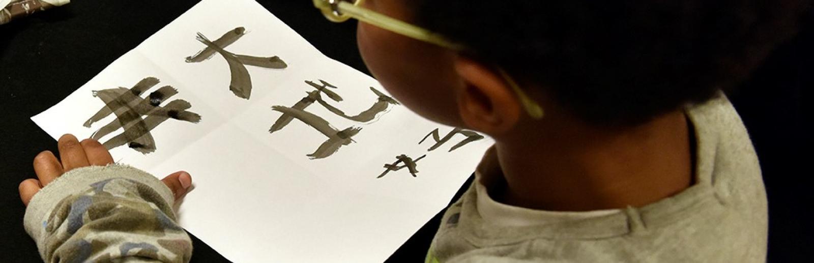 Atelier jeune public, enfant entrain d'écrire à l'encre chinoise 